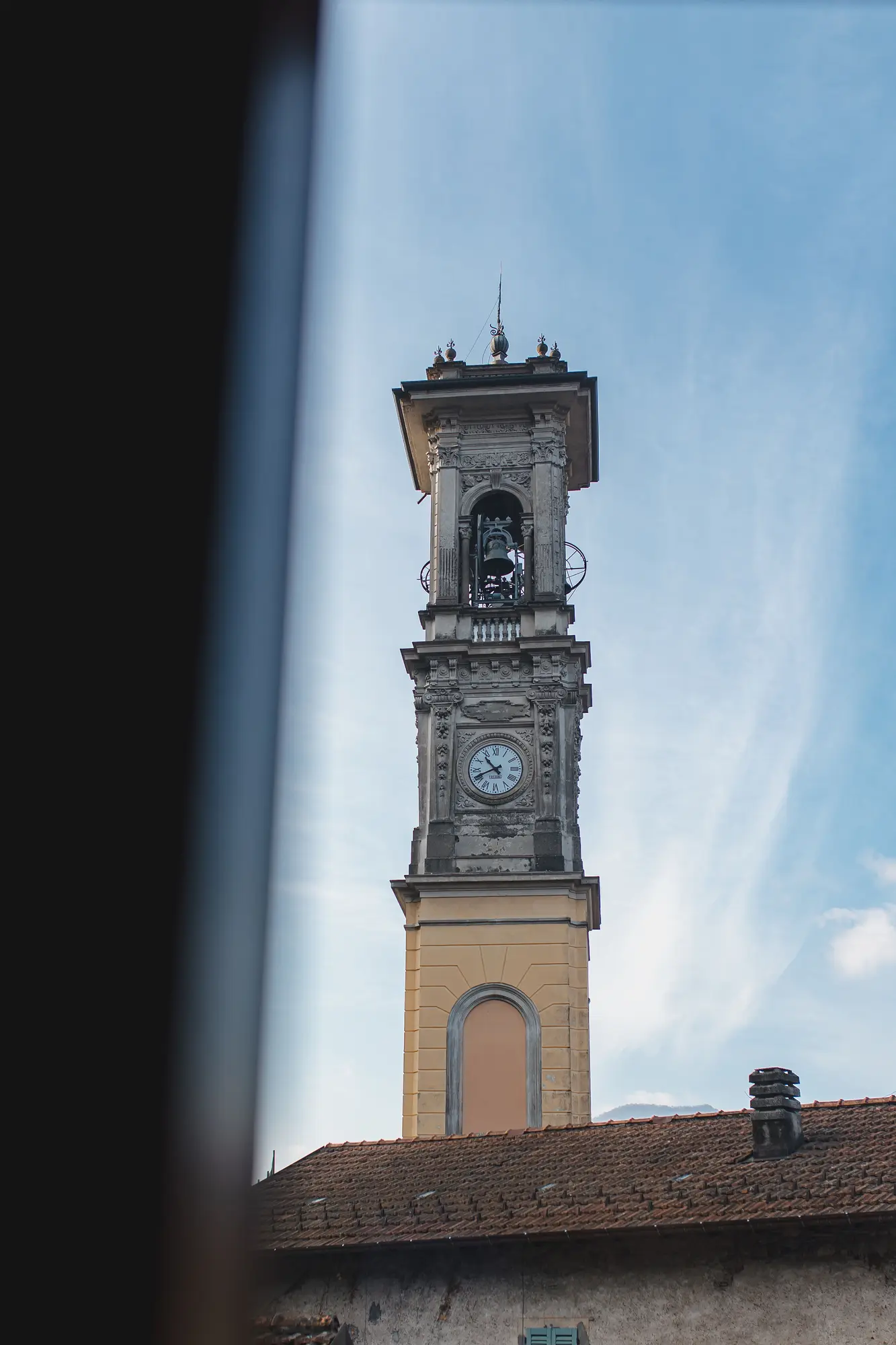 Bell tower of Porto Ceresio church seen through a window against a blue sky